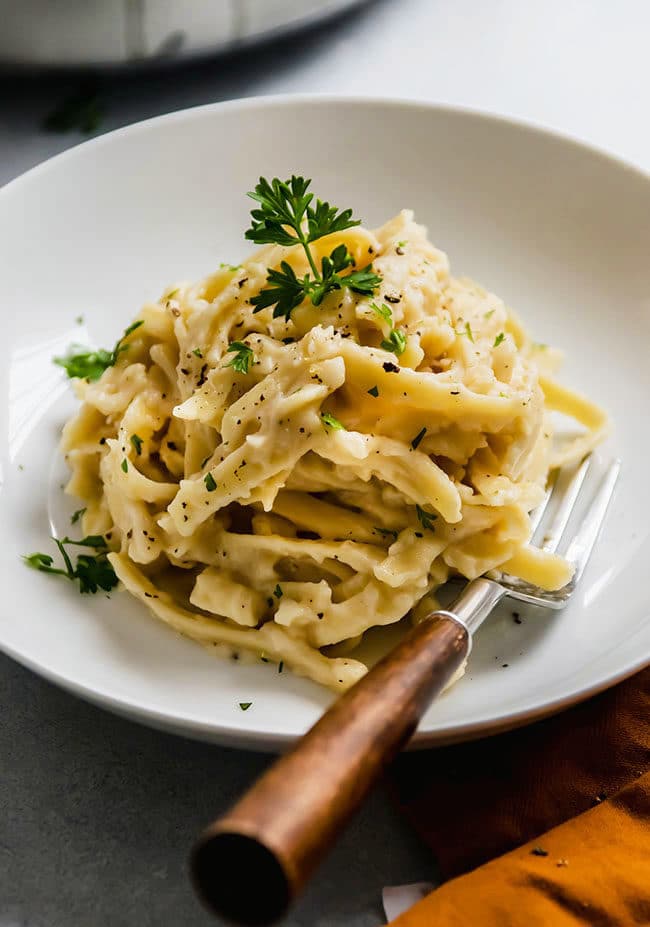 Fettuccine alfredo topped with fresh parsley on a white plate with a wooden fork.