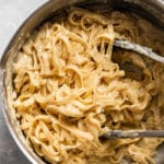 Fettuccine alfredo in a large pot with grey kitchen tongs.