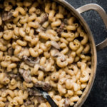 Macaroni and cheese with mushrooms in a silver pot on a black background.