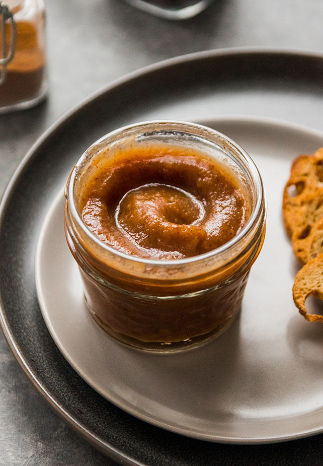 Apple butter in a small mason jar on a grey plate.