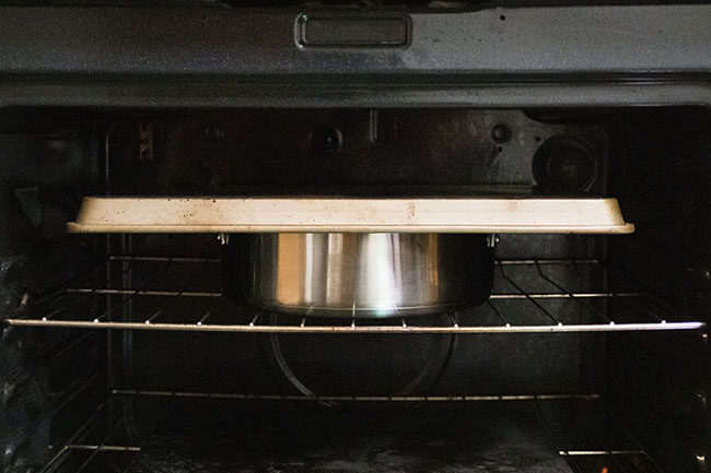 Sheet pan on top of stainless steel pot in an oven.
