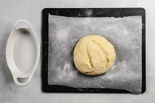 Bread dough on a black cutting board lined with parchment paper.