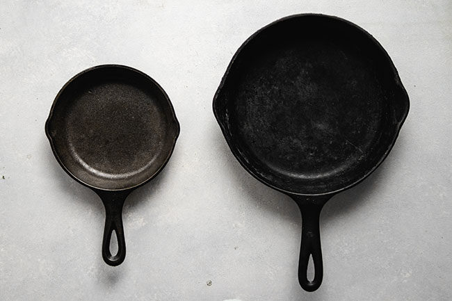 White table with a large cast iron skillet next to a small cast iron skillet.
