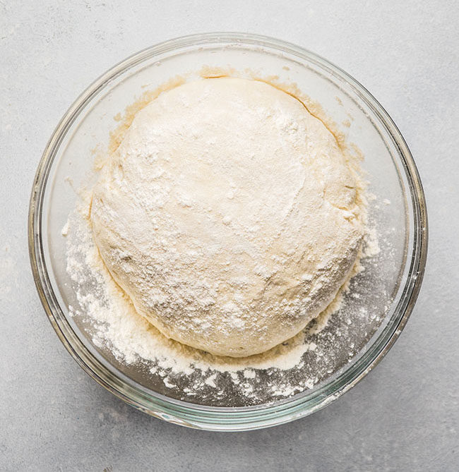 Bread dough in a glass bowl on a white countertop.