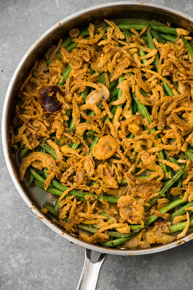 Green bean casserole topped with fried onions in a large metal skillet.