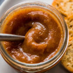 Silver spoon lifting apple butter out of a mason jar.