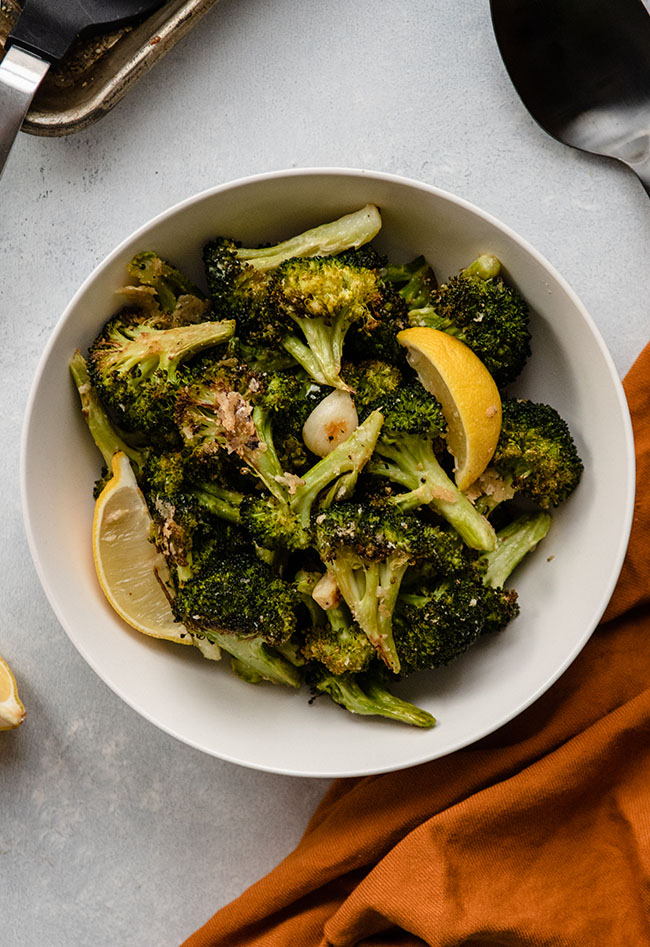 Roasted broccoli and lemon wedges in a white bowl next to a yellow napkin.