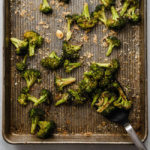 Black spatula lifting roasted broccoli from a sheet pan.