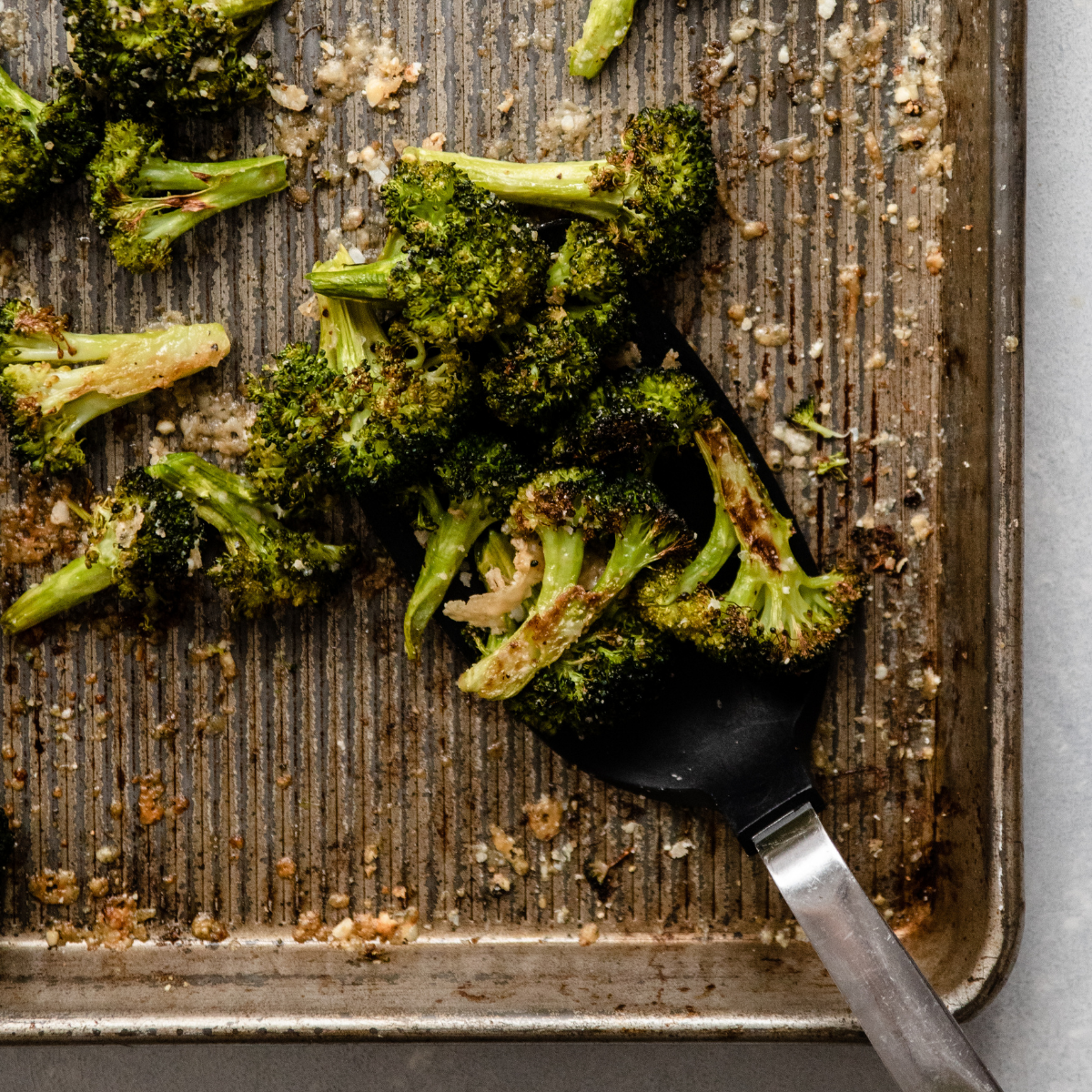 Black spatula lifting roasted broccoli from a sheet pan.