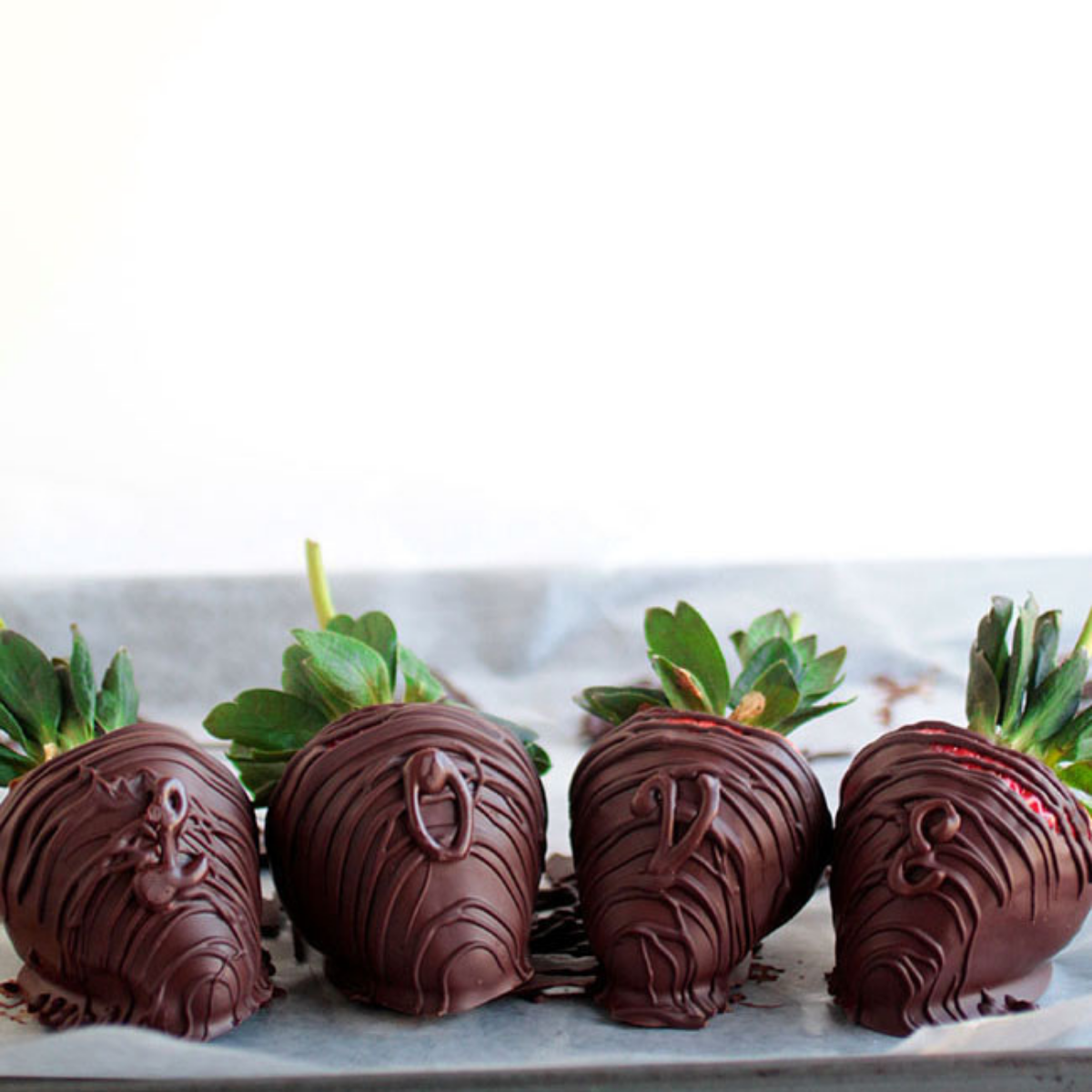 Four chocolate strawberries with chocolate decorations in front of a white background.