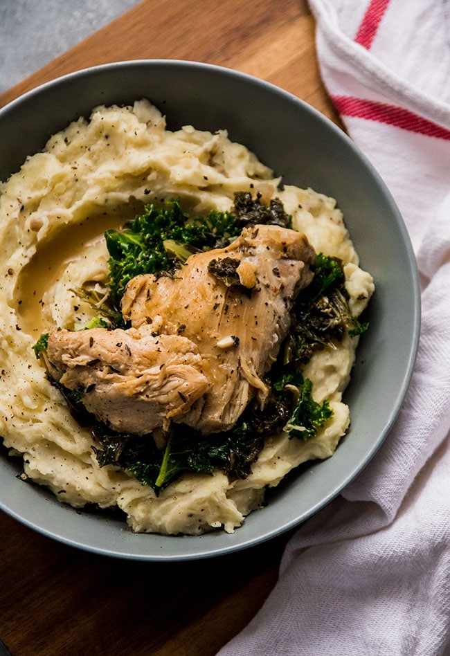 Chicken thighs in a shallow blue bowl with mashed potatoes and kale.