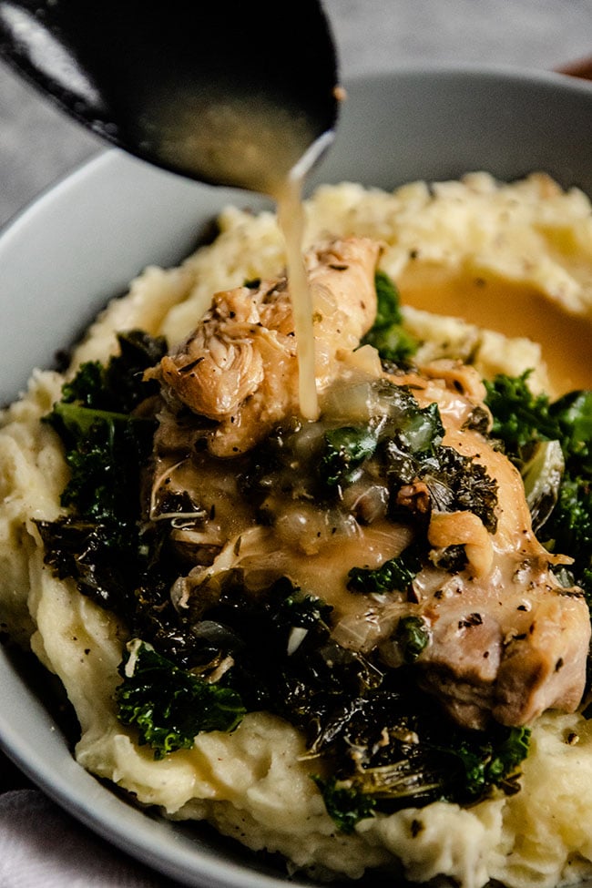 Black spoon drizzling lemon sauce over chicken and kale in a blue bowl.