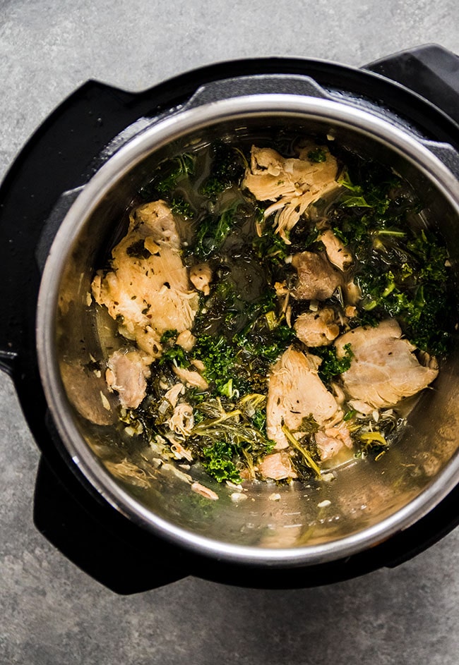 Cooked chicken thighs and kale in the bowl of an Instant Pot.