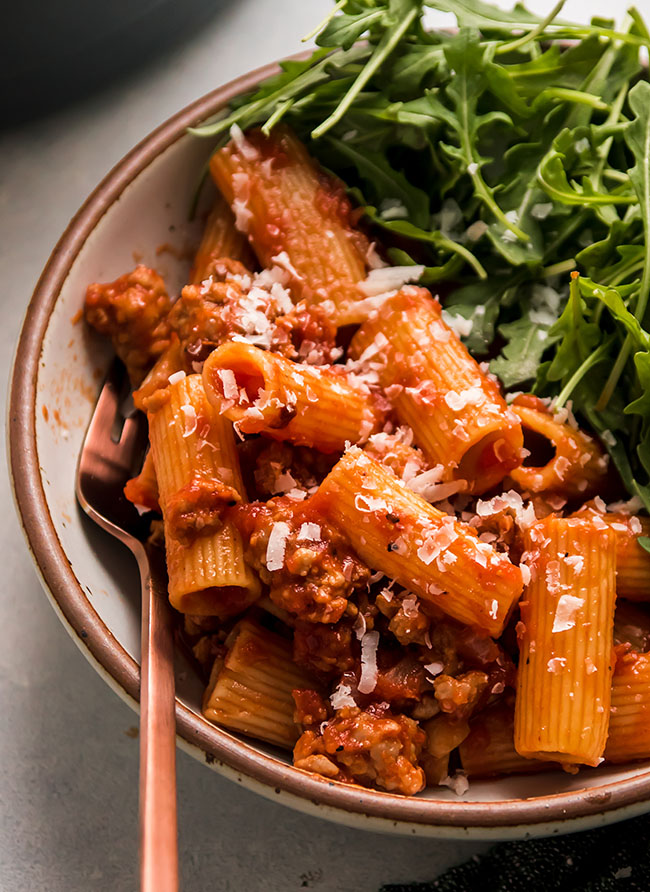 A copper fork taking a bite of rigatoni with tomato sauce.