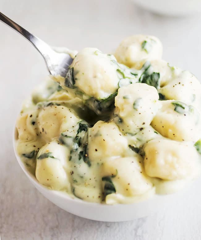 Fork lifting a bite of gnocchi with spinach sauce out of a white bowl.