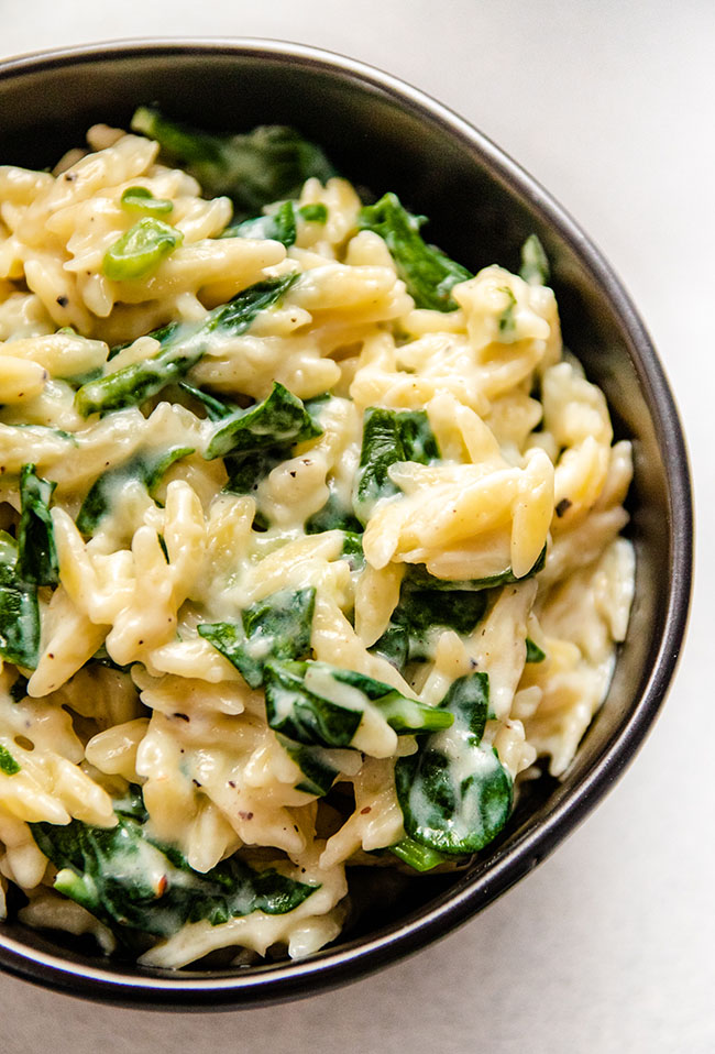 Orzo mixed with fresh spinach in a black bowl.