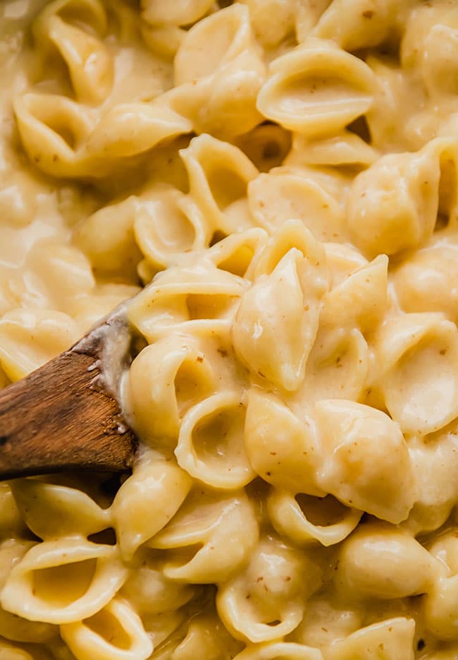 Wooden spoon stirring shell pasta with cheese sauce.