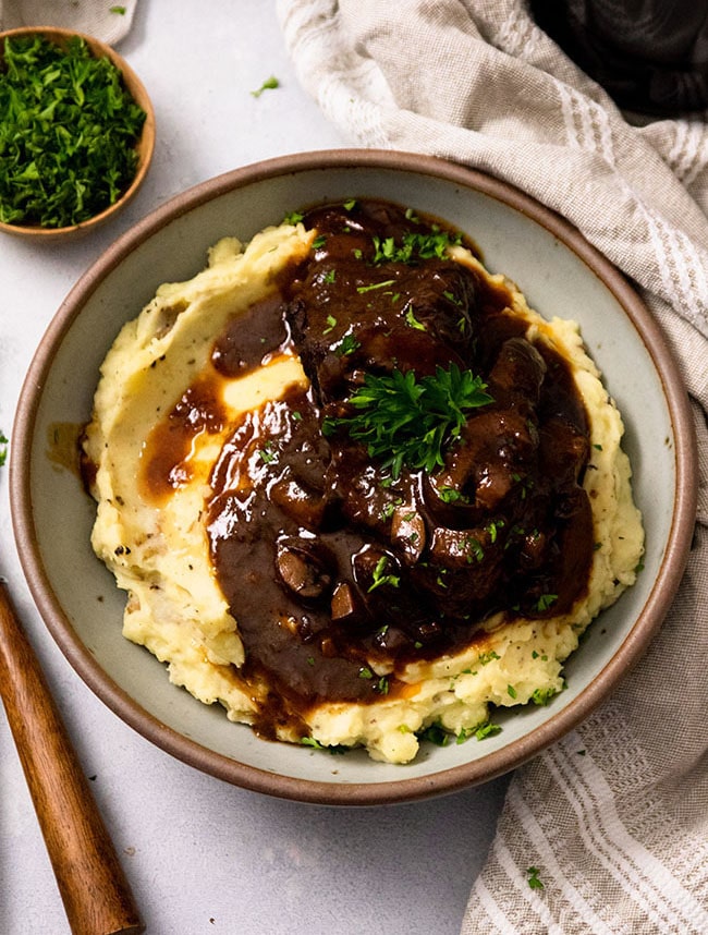 Mashed potatoes and short ribs covered in a red sauce in a large grey bowl.