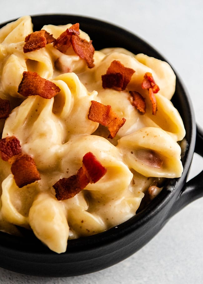 Black baking dish with handles filled with macaroni and cheese and topped with crispy bacon pieces.