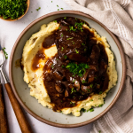 Grey bowl filled with mashed potatoes and short ribs with red wine sauce.