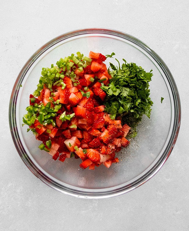 Diced strawberries, cilantro, and jalapeño in a glass bowl.