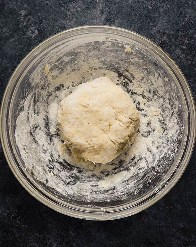 Prepared gnocchi dough in a glass bowl on a black countertop.