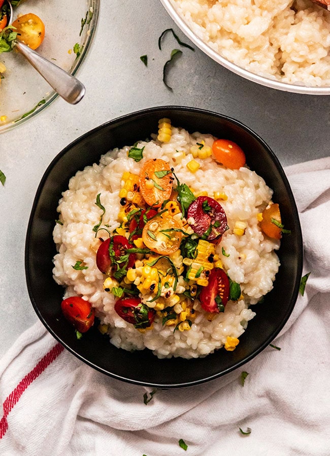 Risotto, corn, and cherry tomatoes in a shallow black bowl.