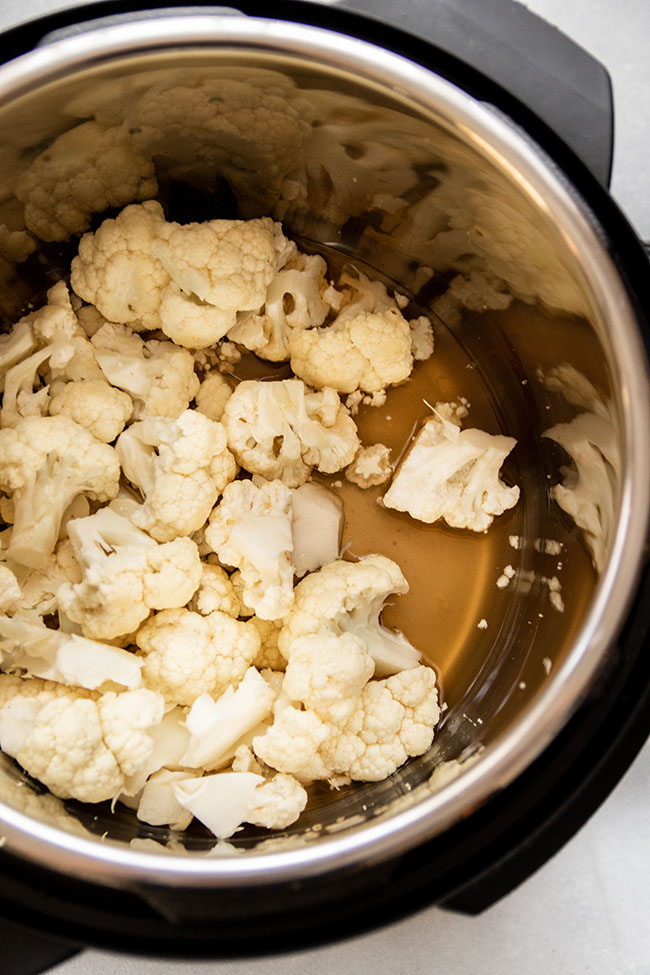 Close up of cauliflower florets and vegetable stock in the bowl of an Instant Pot.