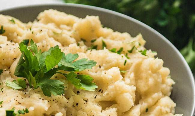 Mashed potatoes topped with fresh parsley in a grey bowl.