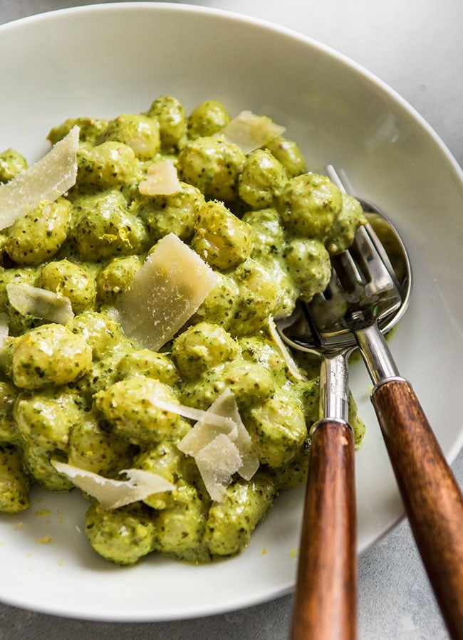 Fresh gnocchi and creamy green pesto sauce in a white bowl with a wood-handled fork on the side.