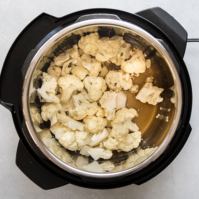 Cauliflower florets and vegetable stock in the bowl of an Instant Pot.