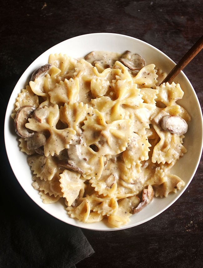 White bowl filled with bowtie pasta and mushroom cream sauce on a dark brown table.