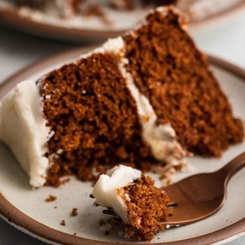 Copper fork holding a bite of a layered spice cake with white frosting.