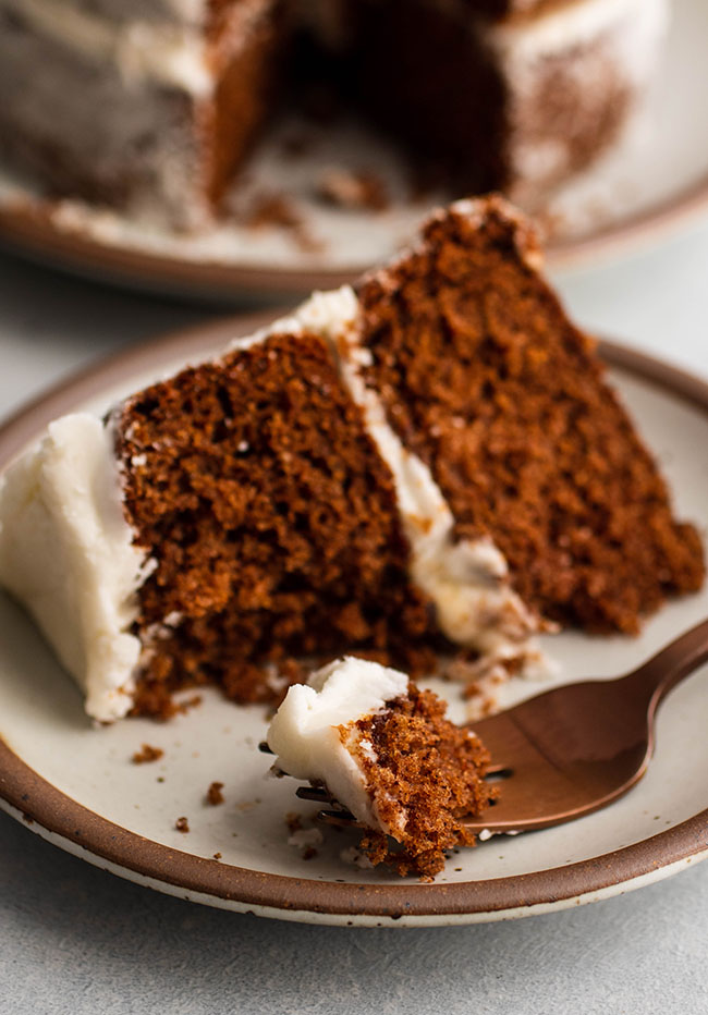 Slice of brown apple butter cake with white frosting, with a copper fork cutting one bite off the end.