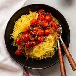 Shallow black bowl filled with spaghetti squash and roasted tomatoes.