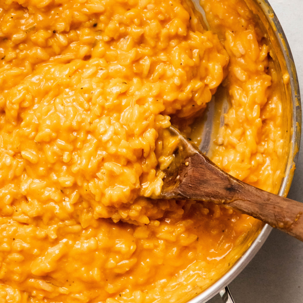 Wooden spoon stirring butternut squash puree into risotto.