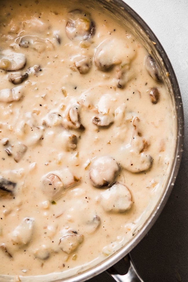 Cream sauce with mushrooms in a shallow silver skillet.