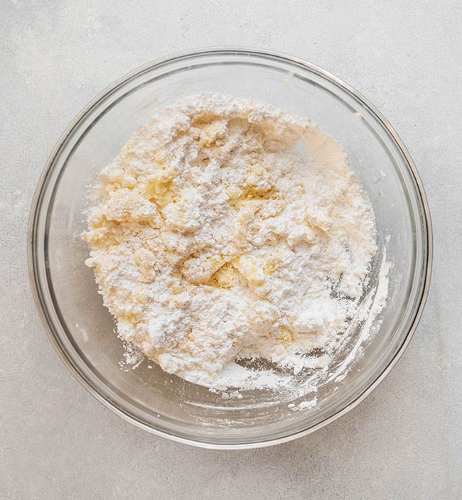 Powdered sugar and small pieces of butter in a glass bowl.