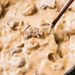 Copper spoon stirring creamy mushroom sauce in a shallow skillet.