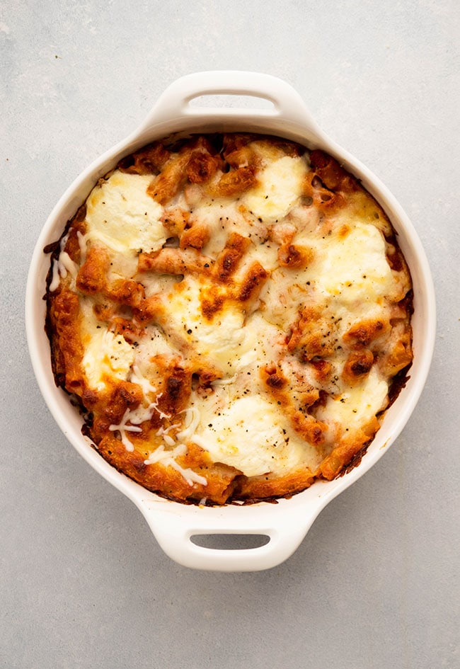 Baked ziti in a round white baking dish with handles.