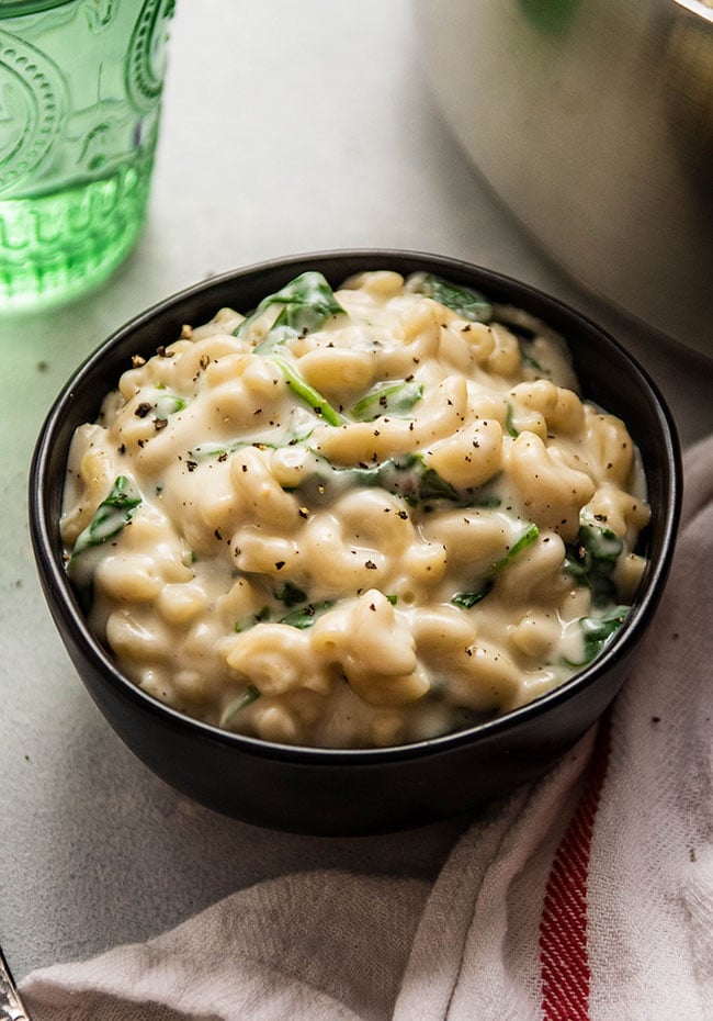 Creamy macaroni pasta with spinach in a black bowl.