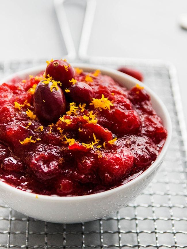 Cranberry sauce topped with orange zest in a white bowl next to a window.