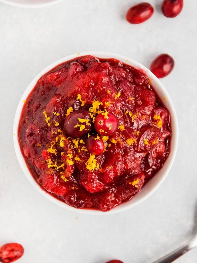Cranberry sauce in a white bowl, surrounded by several fresh cranberries.