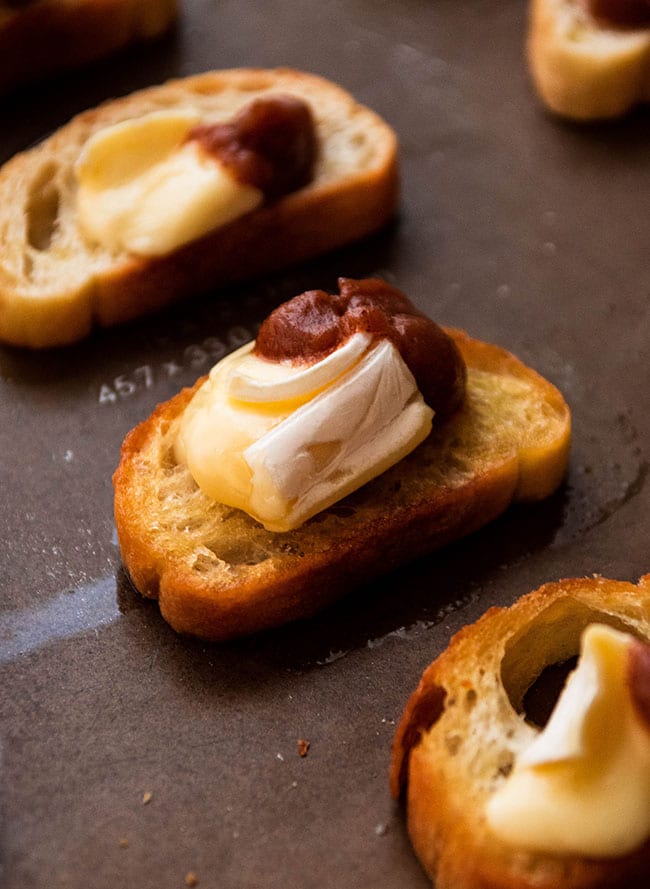 Dark metal sheet pan with four crostini pieces topped with brie and apple butter.