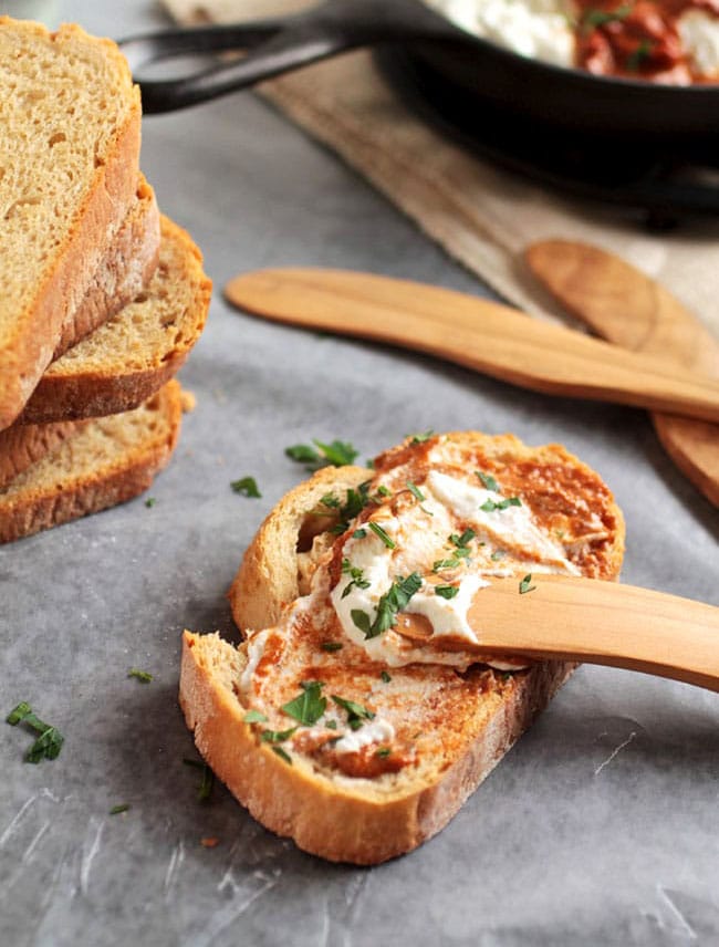 Wooden knife spreading baked ricotta dip on a piece of toast.
