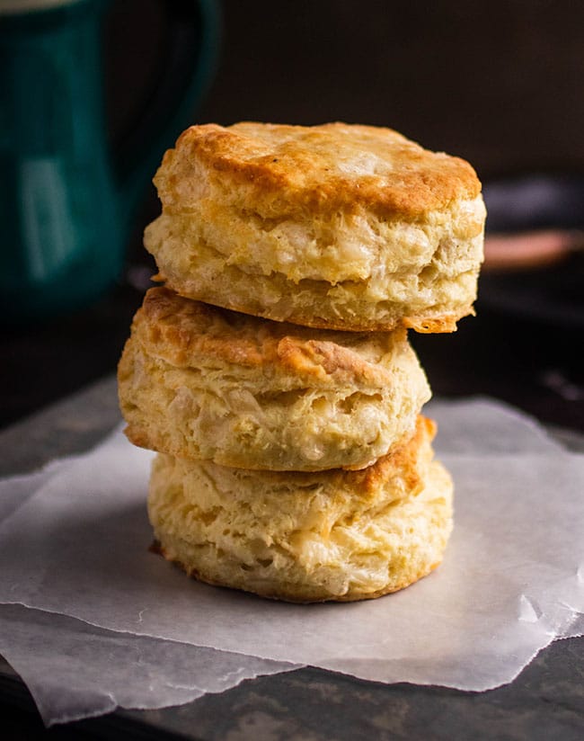 Stack of three gruyere biscuits on a piece of parchment paper in front of a green mug.