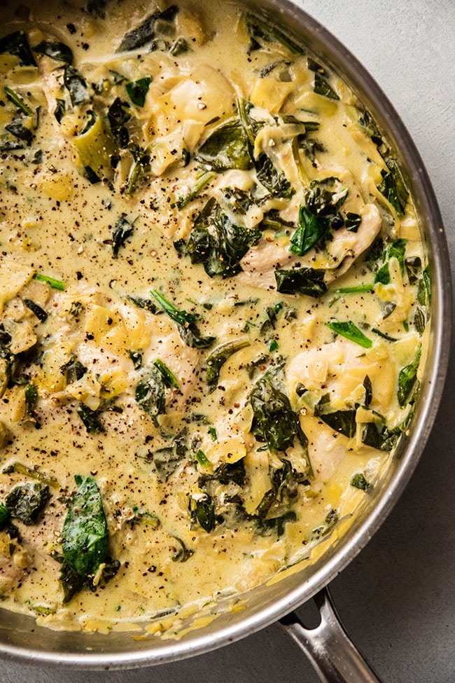 Skillet filled with chicken breasts in a spinach cream sauce.