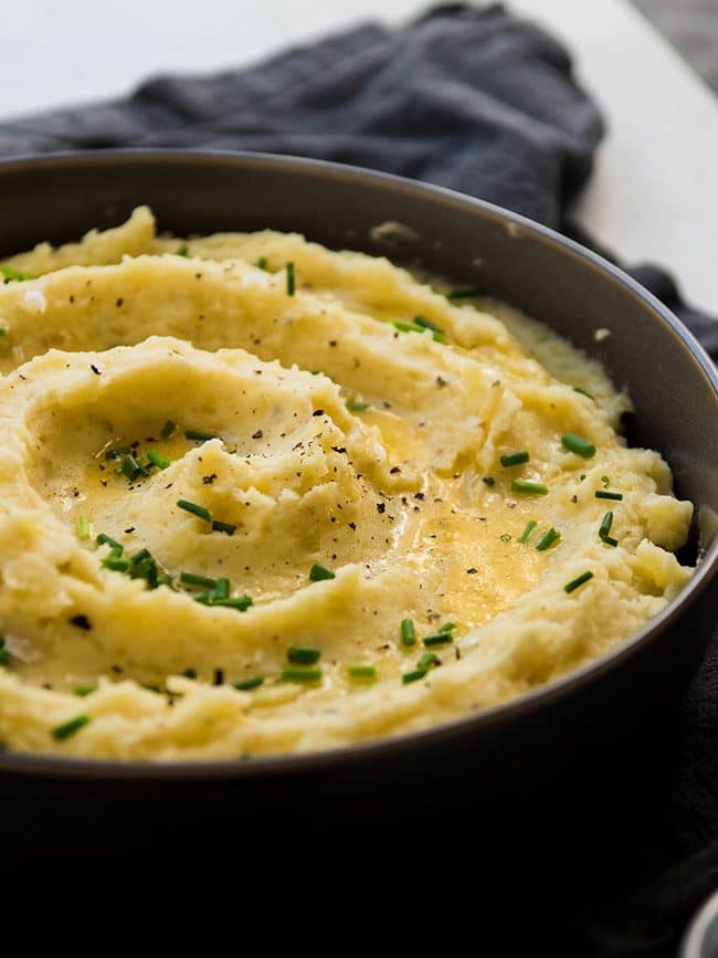 Mashed potatoes in a grey bowl, topped with melted butter and fresh chives.