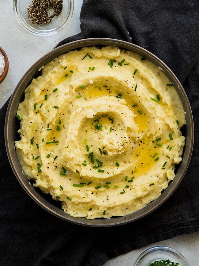 Shallow grey bowl filled with mashed potatoes and topped with fresh chives and drizzled with melted butter.