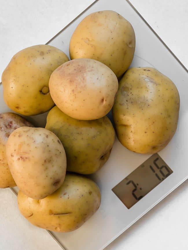 Several yellow potatoes sitting on top of a silver kitchen scale.